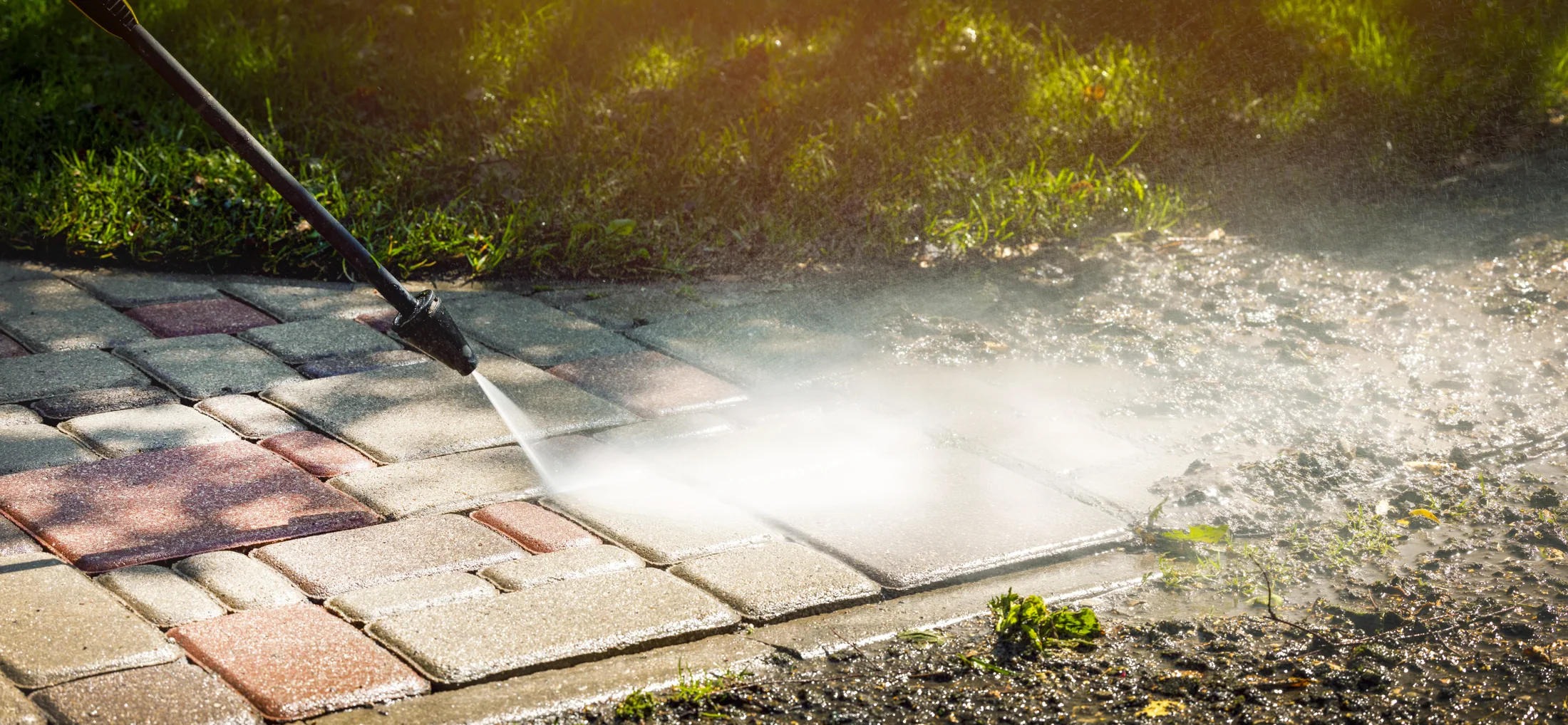Illustrative stock photograph of a water jet cleaning block paving in sunlight.