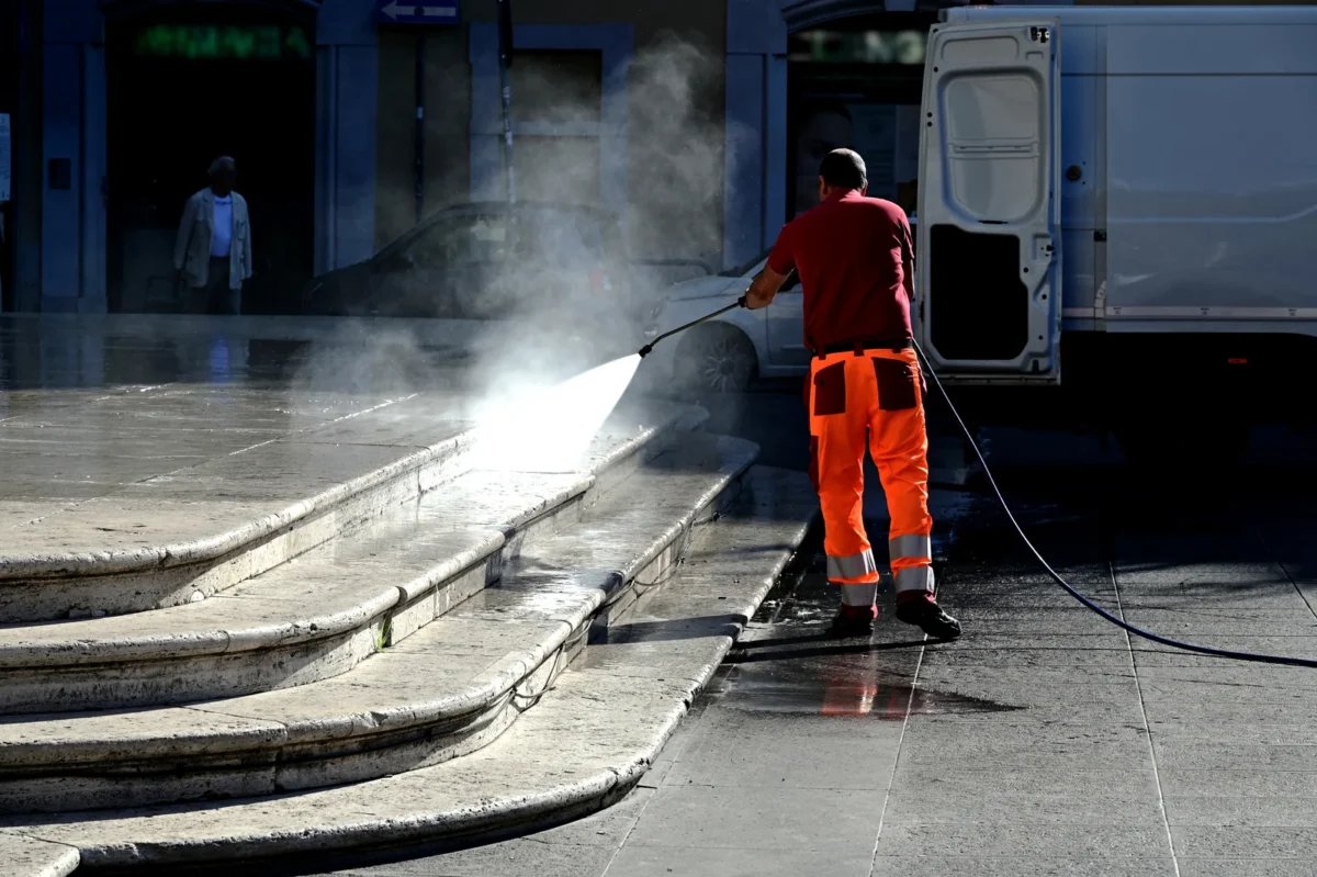 Worker pressure washing stone steps in strong sunlight