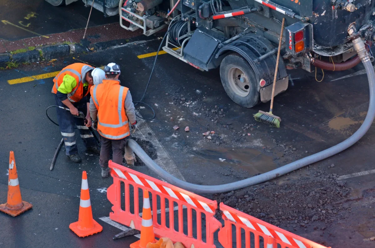 Road drainage crew working beside a vacuum tanker inside a barriered work area