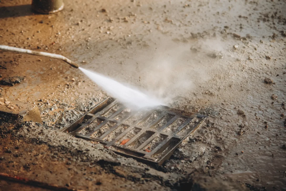 Water jet cleaning construction dirt from a drainage gully grating.