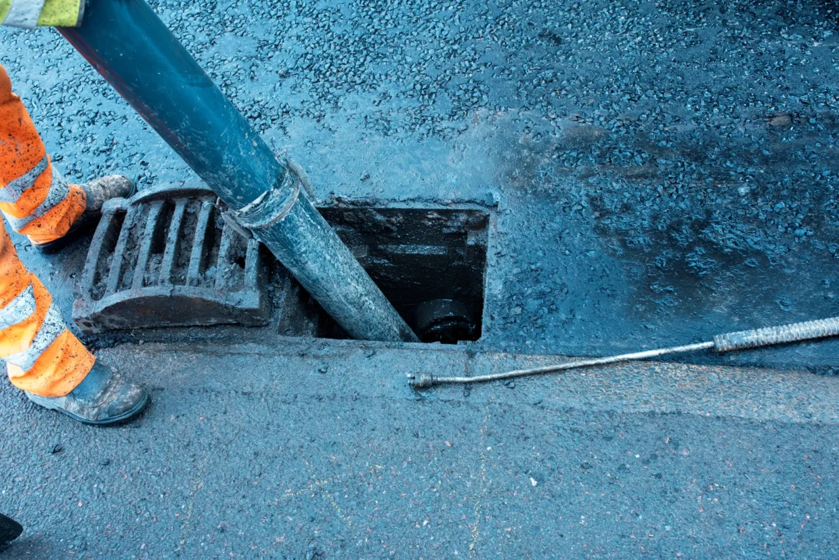 A suction hose clearing a road gully beside its removed grate.